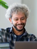 Portret van Laurent, man met grijs krullend haar en baard, glimlachend achter laptop