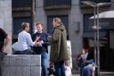 Twee mannen staan bij een vrouw zittend op een stenen rand en interviewen haar